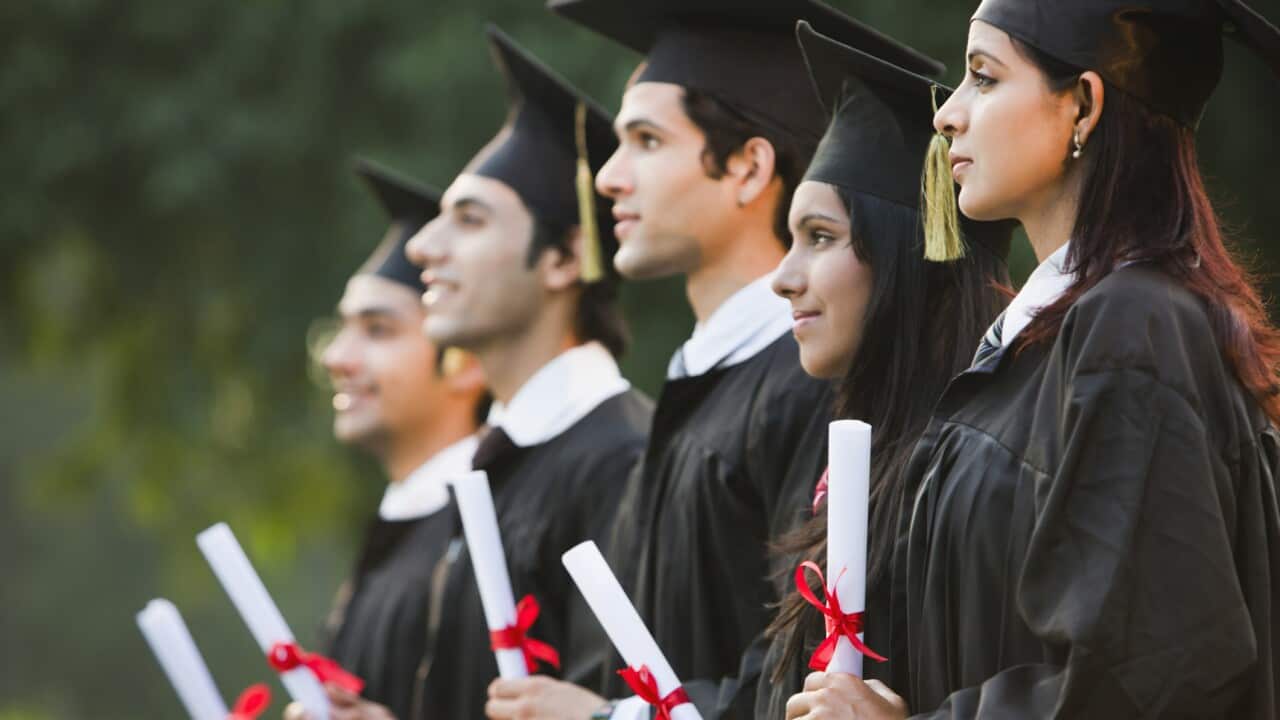 Students in graduation gowns holding diplomas