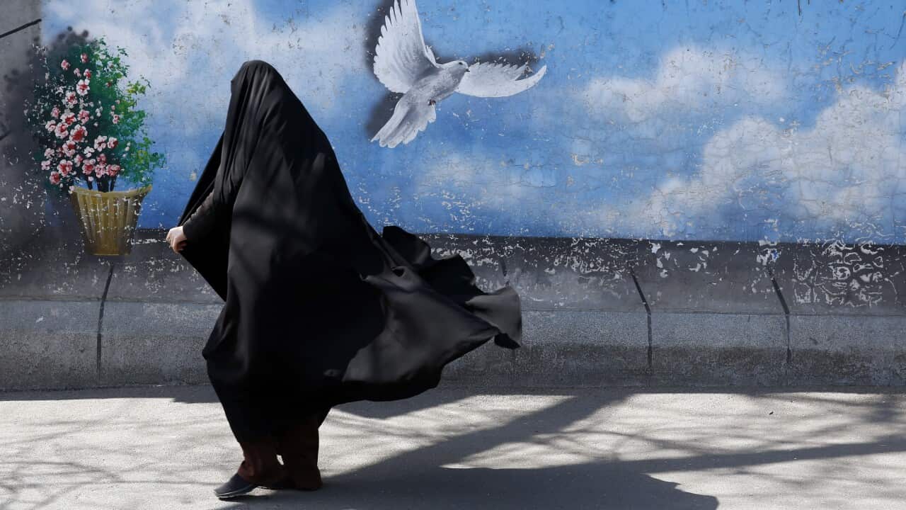 An Iranian woman walks past a wall painting of a peace bird at a street in downtown Tehran, Iran.