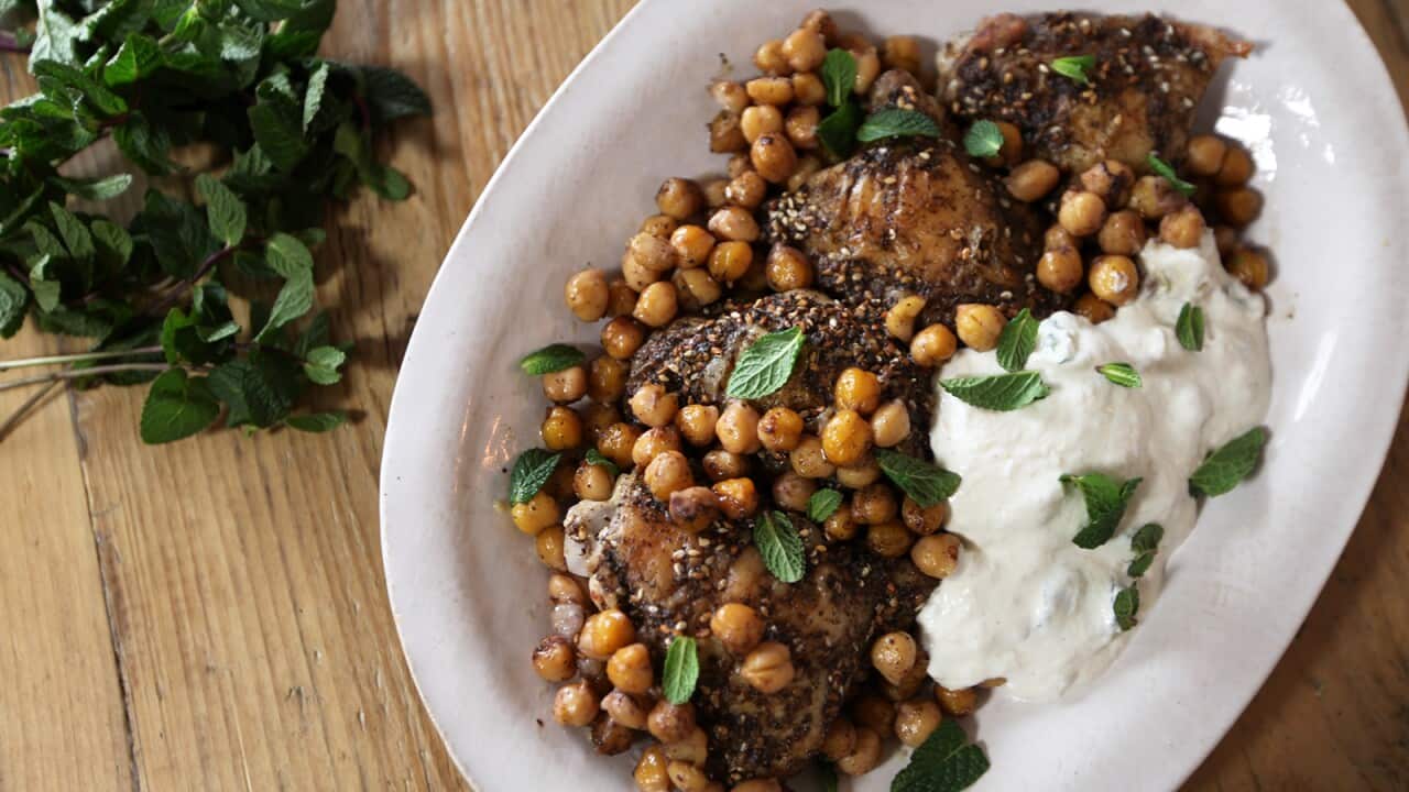 Pieces of cooked chicken sit on a platter in a bed of chickpeas, with a large dollop of yoghurt alongside.