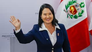 A lady in a blue blazer waves and smiles.