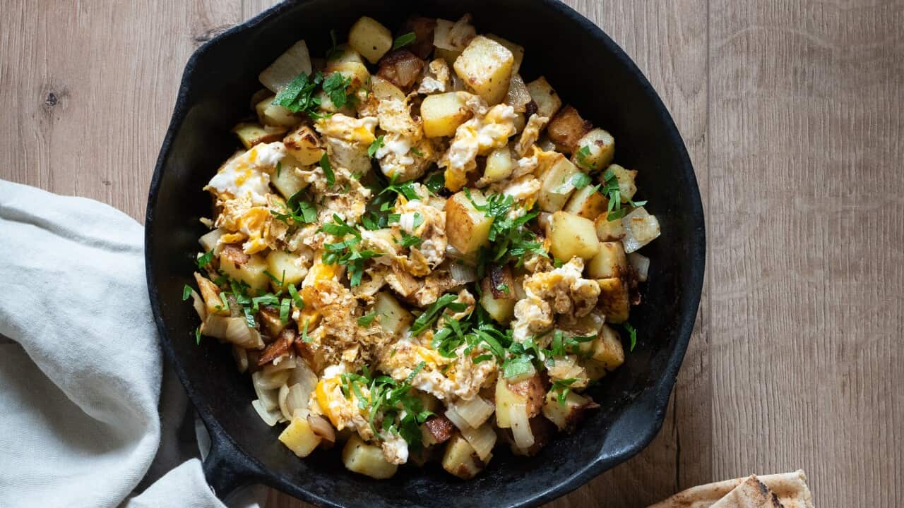 Scrambled eggs on a potato and onion hash, flavoured with Lebanese 7 spice. It's served in a black cast iron pan, with lebanese flatbread, olives, and pickles on the side.
