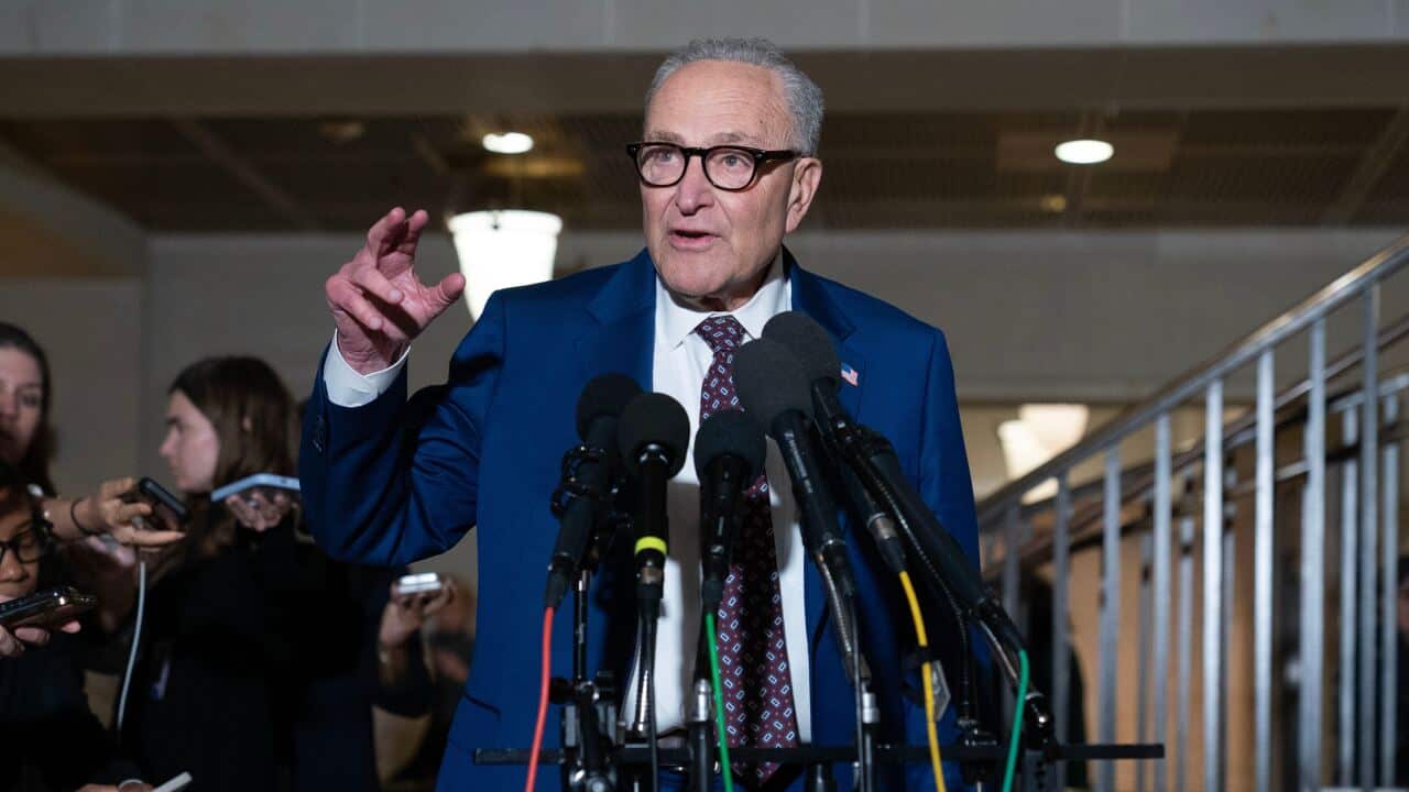 A man in a blue suit stands in front of microphones.