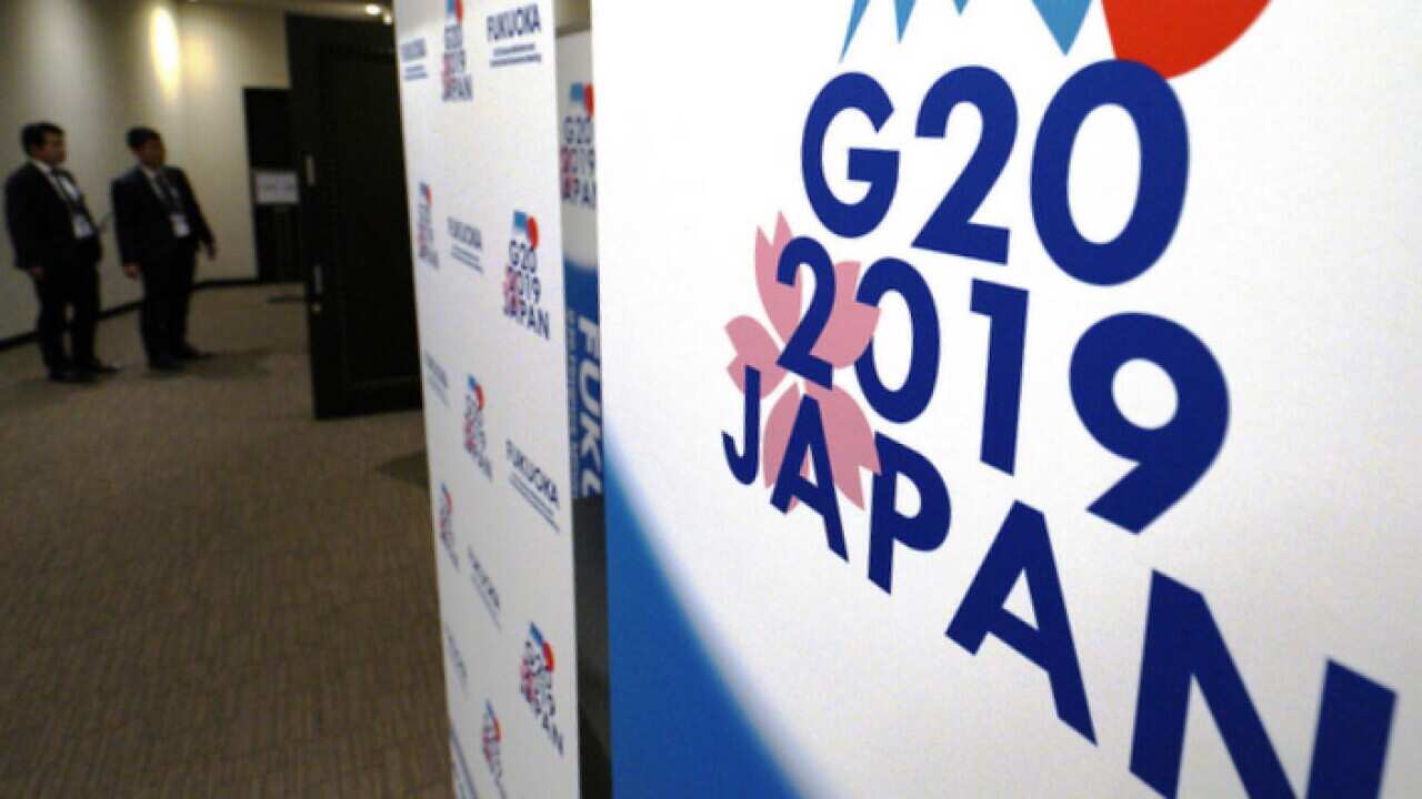 Staff members stand near the emblem of G20 2019 Japan at the entrance of the press centre