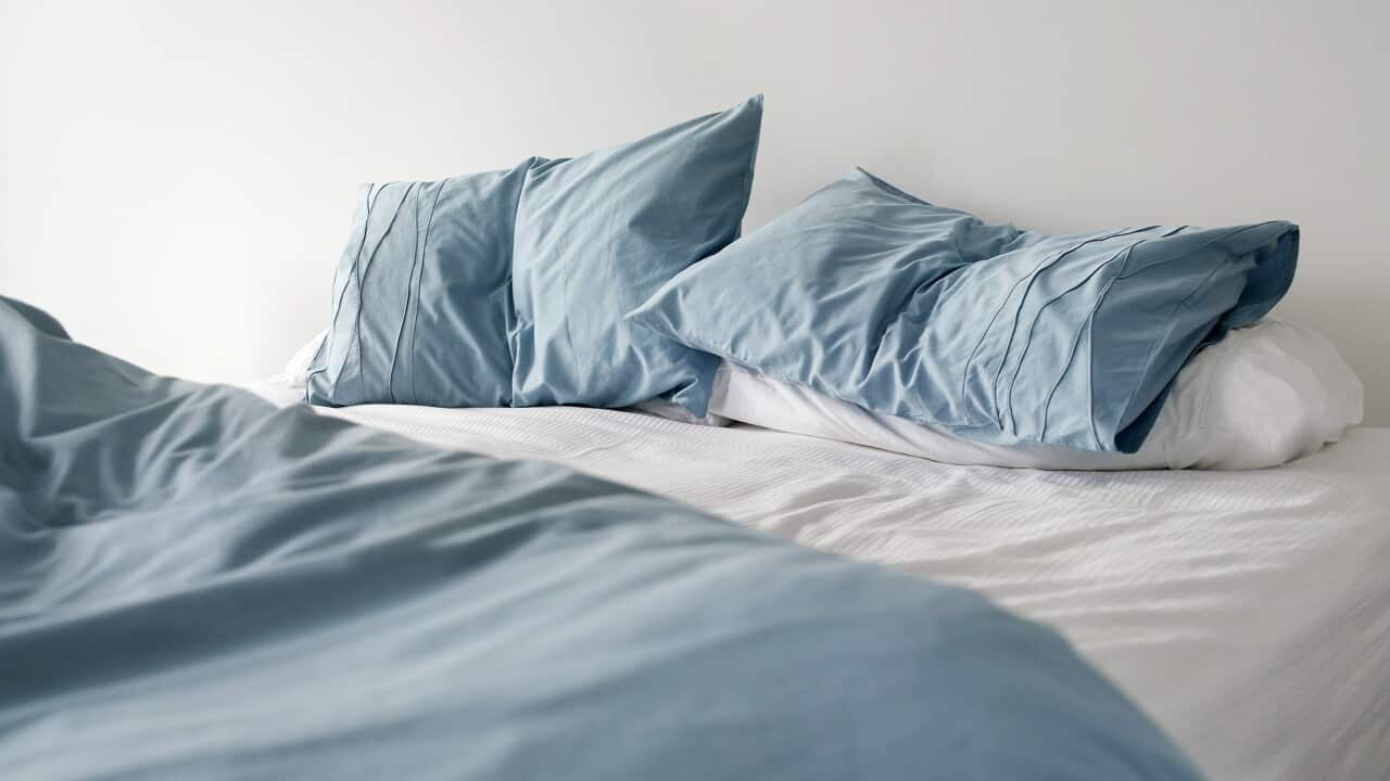 Morning view of an unmade bed with crumpled blue bed linens and no people