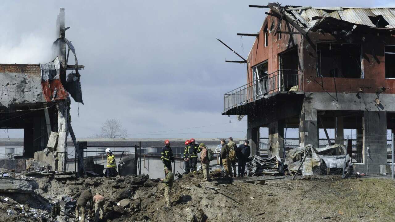 Ukrainian servicemen and firefighters stand next to a tyre shop destroyed by an airstrike in Lviv, Ukraine.
