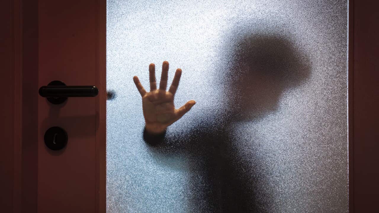 Blurred sad boy leaning open hand against glass door.