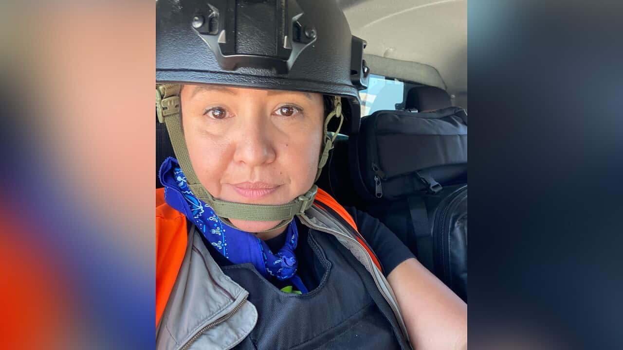 A woman wearing a helmet and orange vest sits in a car seat.