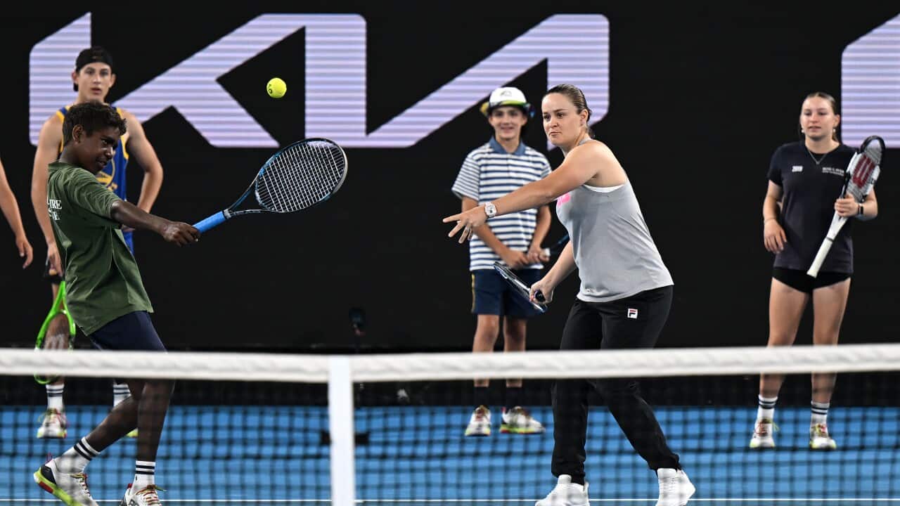 ash barty in casual clothes on a tennis court demonstrates a stroke to a young boy, who has just hit a tennis ball