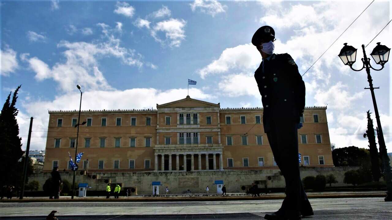 A police officer wearing protective gloves stands guard in front of the Greek parliament, Athens.