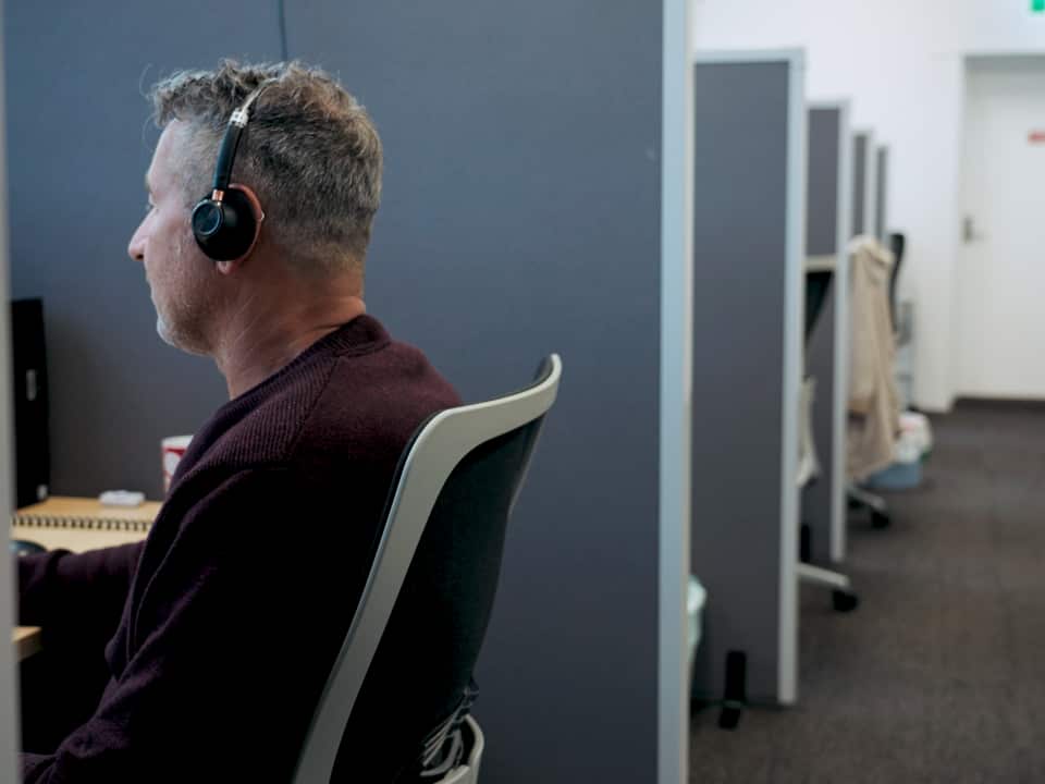 A man sits at his desk with headphones on.