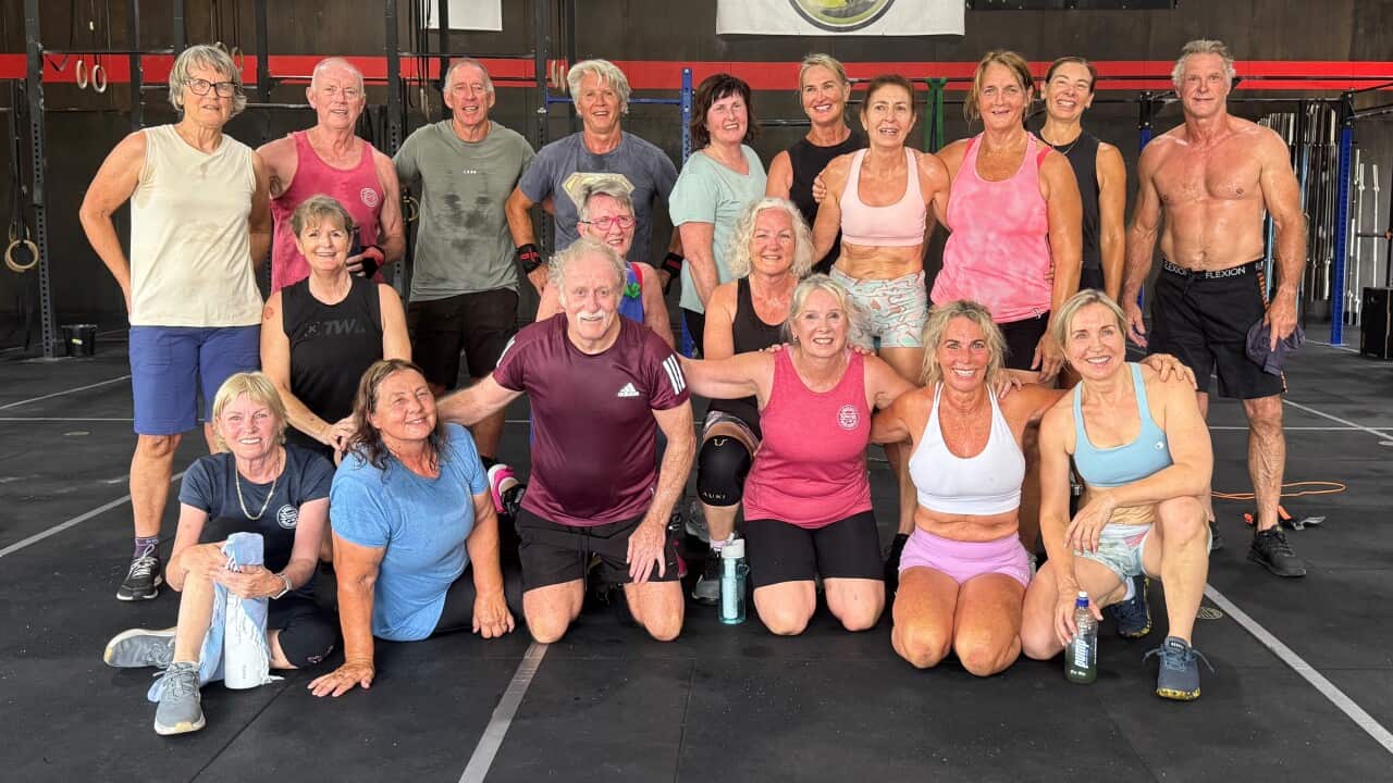 A group of people wearing sports clothes stand and sit inside a gym.