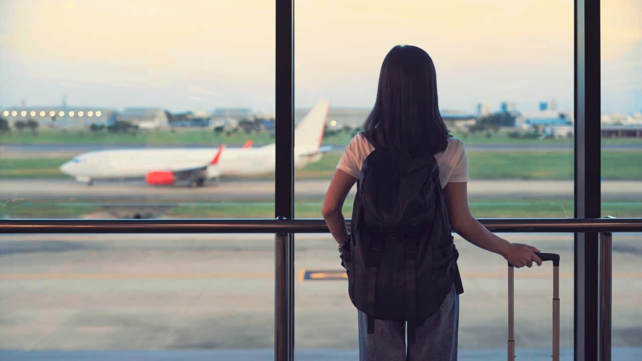 Travel tourist standing with luggage watching sunset at airport window. Woman looking at lounge looking at airplanes while waiting at boarding gate before departure. Travel lifestyle. Transport and travel concept