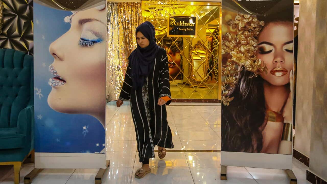 A woman wearing a hijab walks between two beauty banners