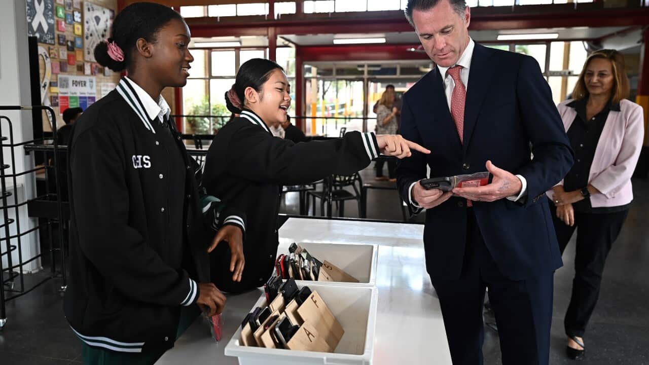 New South Wales Premier Chris Minns learns how to check a phone in during a visit to Condell Park High School. Students are shown on the left-hand side of the image.