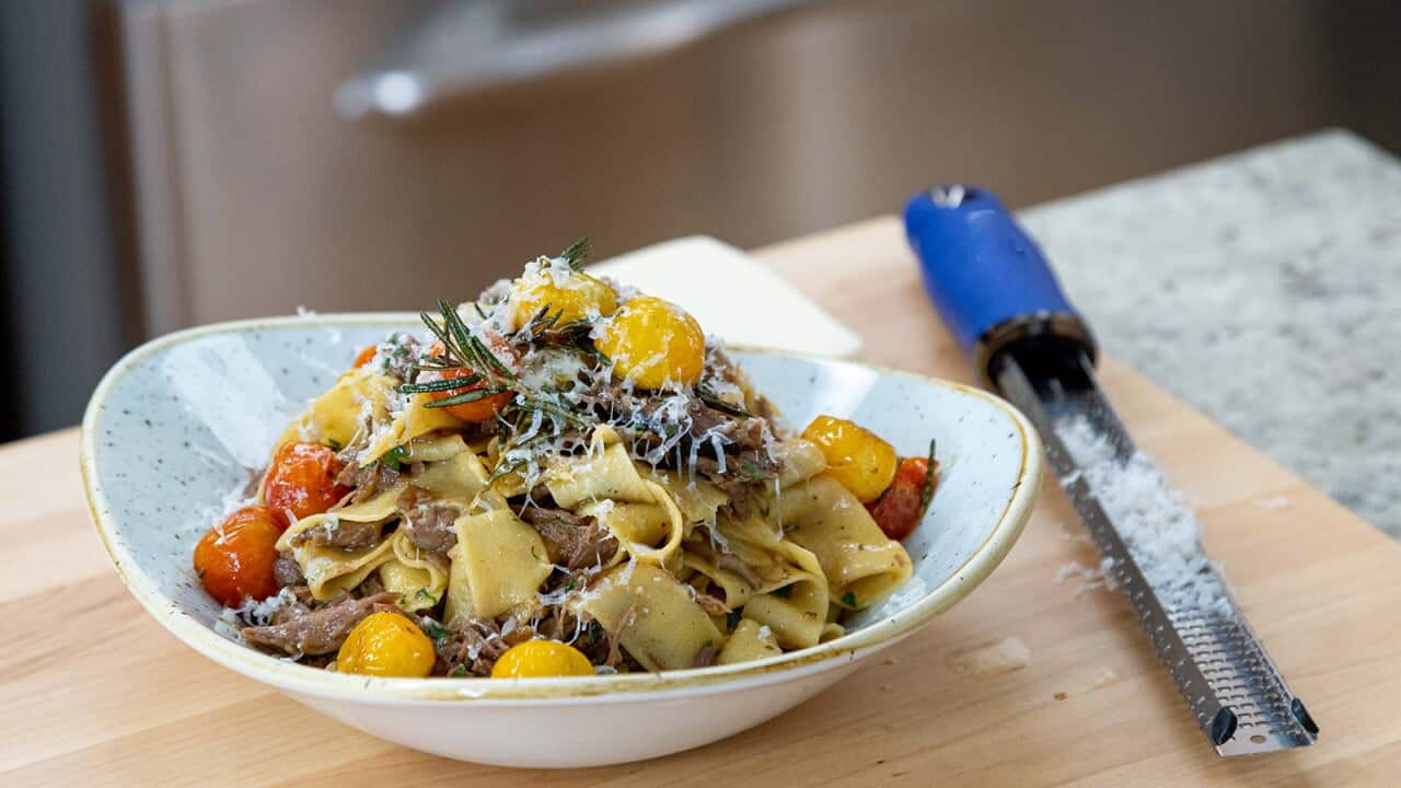 Thick pasta with a meat sauce, topped with yellow and red cherry tomatoes and grated parmesan, sits piled in a lovely speckled blue bowl.