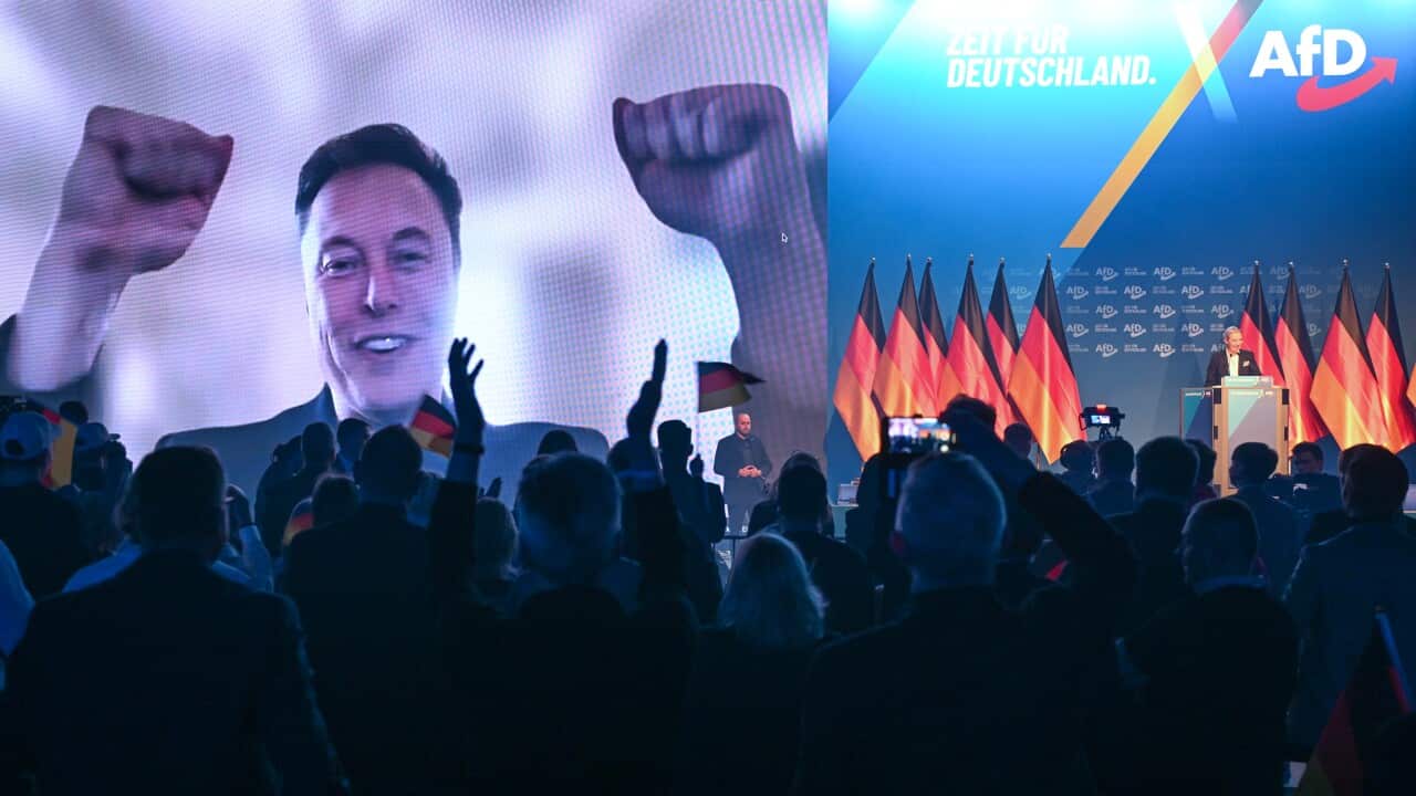 A man with raised fists on a video screen in front of an audience