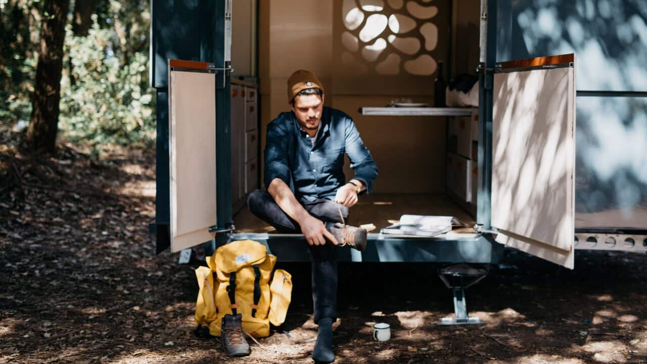 Man with backpack sits outside tiny house