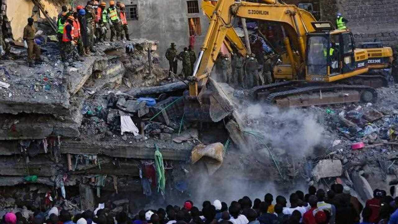 Local residents look at a collapsed building across the river as rescue operations continue in the Huruma estate of the Mathare slum, Nairobi, Kenya