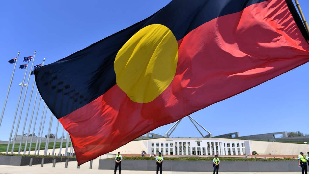 A marcher holds a flag as he protests for Aboriginal rights on Australia Day at Parliament House in Canberra, Sunday, January 26, 2020. (AAP)