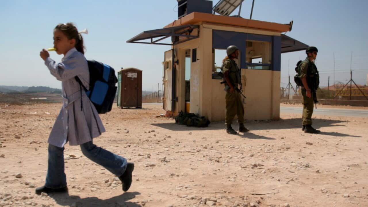A Palestinian schoolgirl crosses a border fence from Ras Atiyah into Ras al-Tirah as she passes Israeli soldiers at a checkpoint