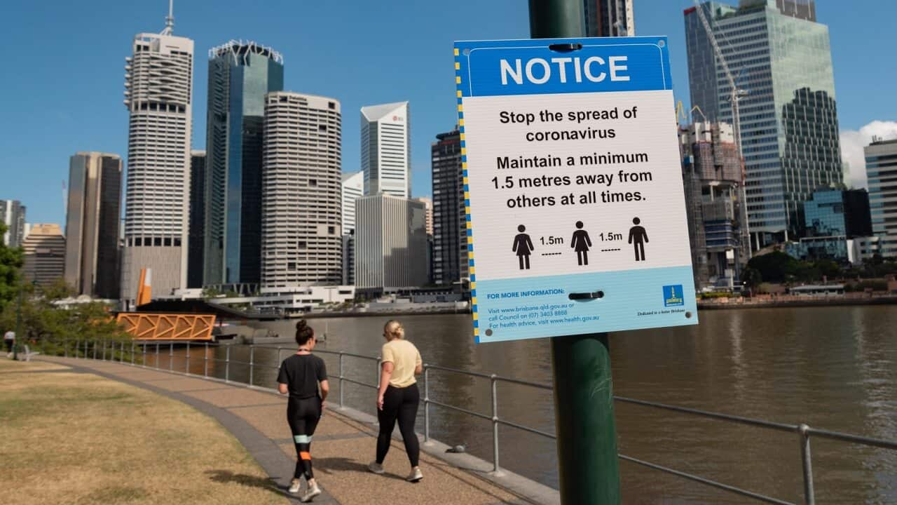 Two ladies walk past a sign warning about social distancing and the Coronavirus pandemic