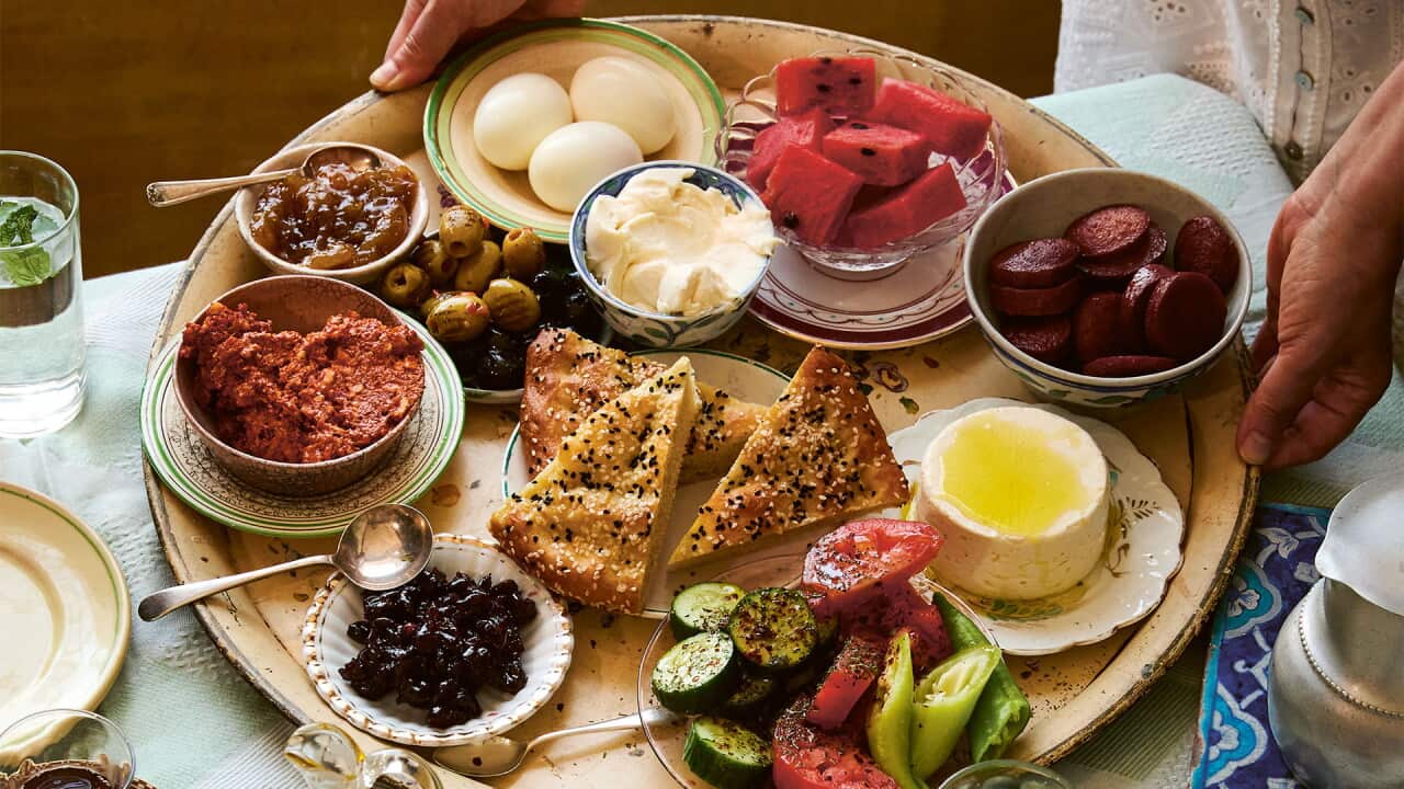 A round platter full of small dishes of food, bread, cheese and eggs is placed onto a table.