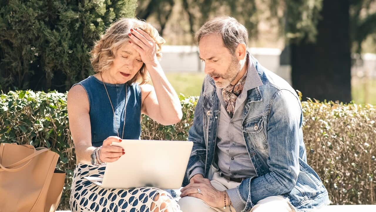 Senior couple looking sad and disappointed while using a laptop in a sunny park