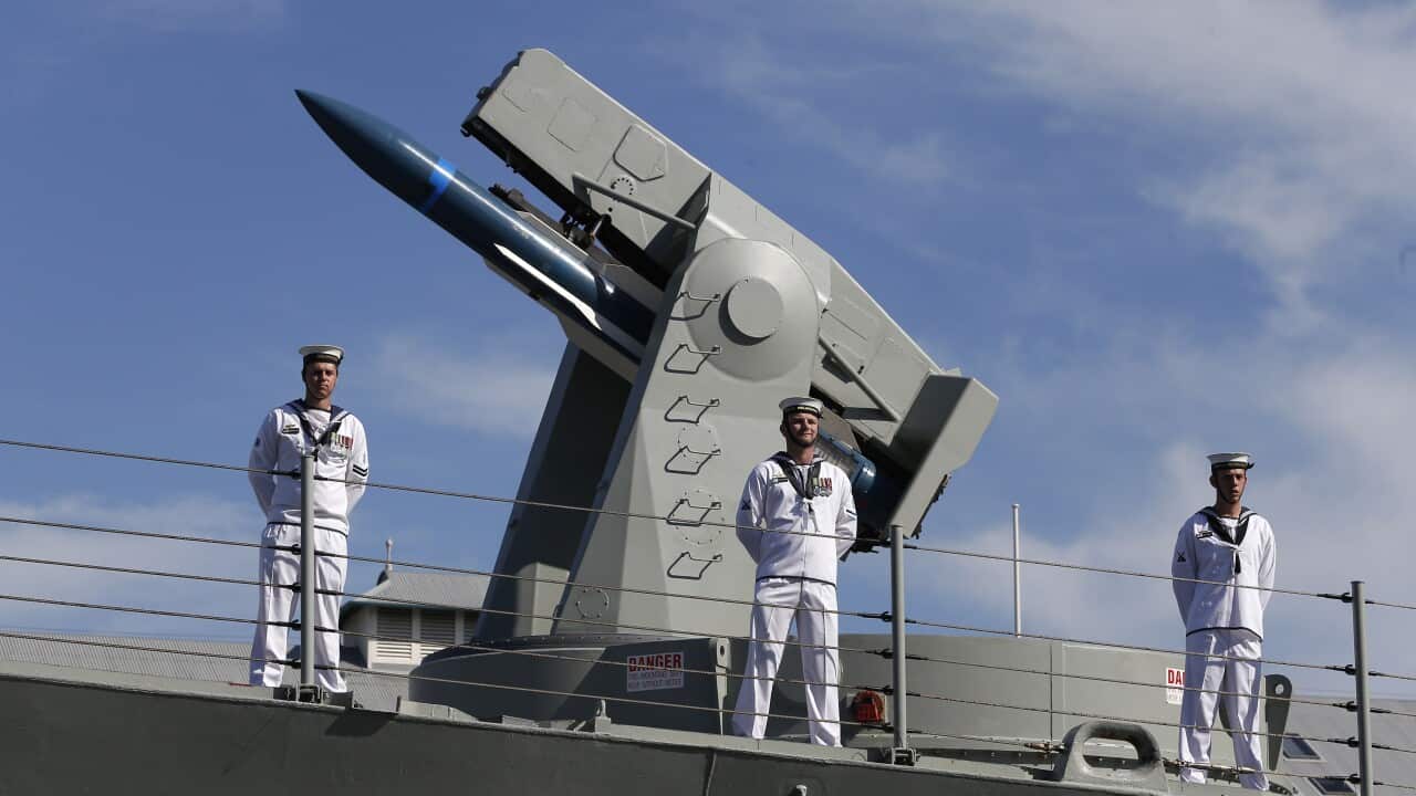Navy personnel standing on a frigate in front of a missile launcher.