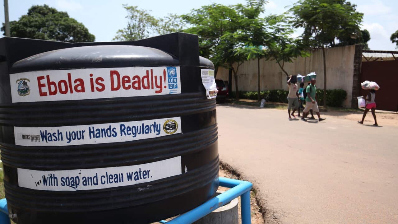 Liberians walk pass a public tank filled with chloronated water to curb the spread of the deadly ebola virus in Monrovia, Liberia.