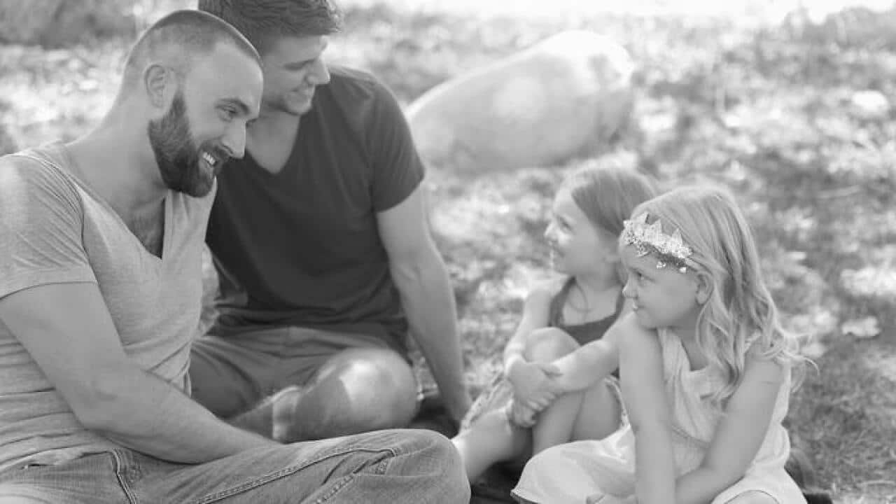 Two sisters and fathers sitting chatting in park