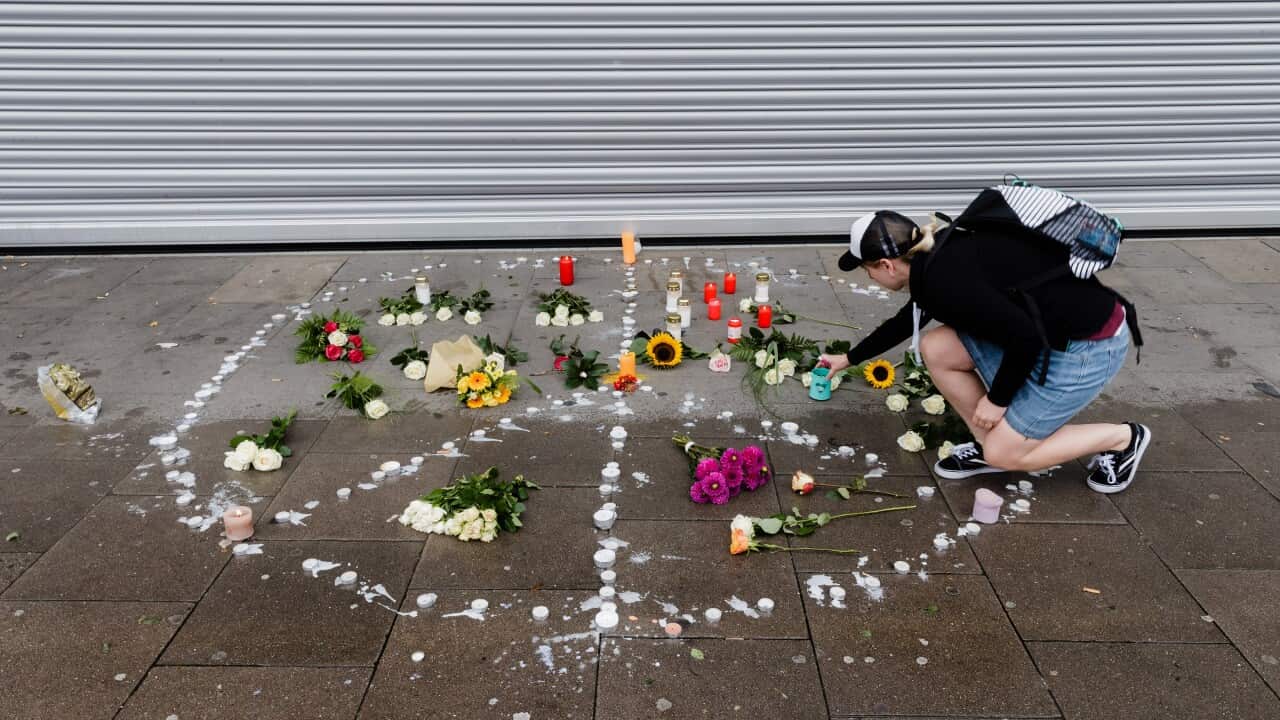 A woman puts a tea light in a peace sign on the pavement in front of the supermarket where a man killed one person and injured six others in Hamburg, Germany.
