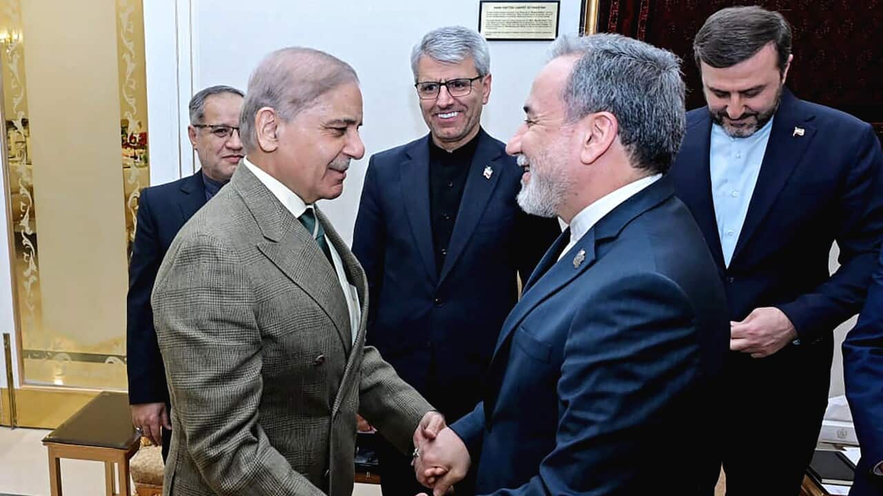 Two men in suits hold hands to greet each other with three other men in suits standing beside them