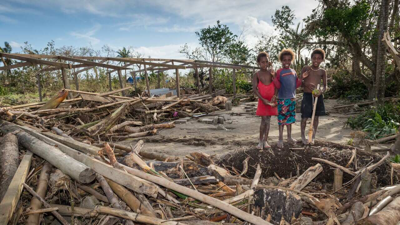 Children stand around the remains of a local community centre destroyed in the cyclone that hit Vanuatu