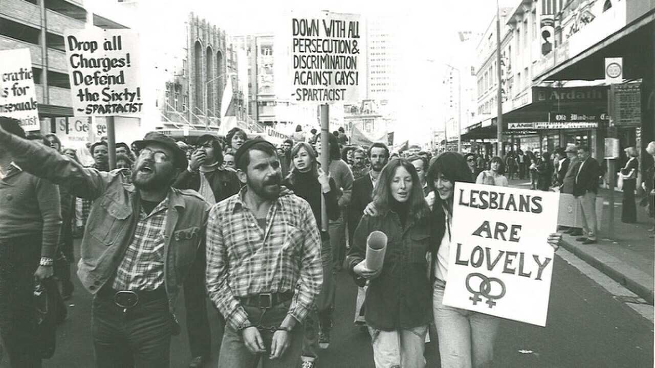 A balck and white photo of people marching and holding up signs with gay rights messages
