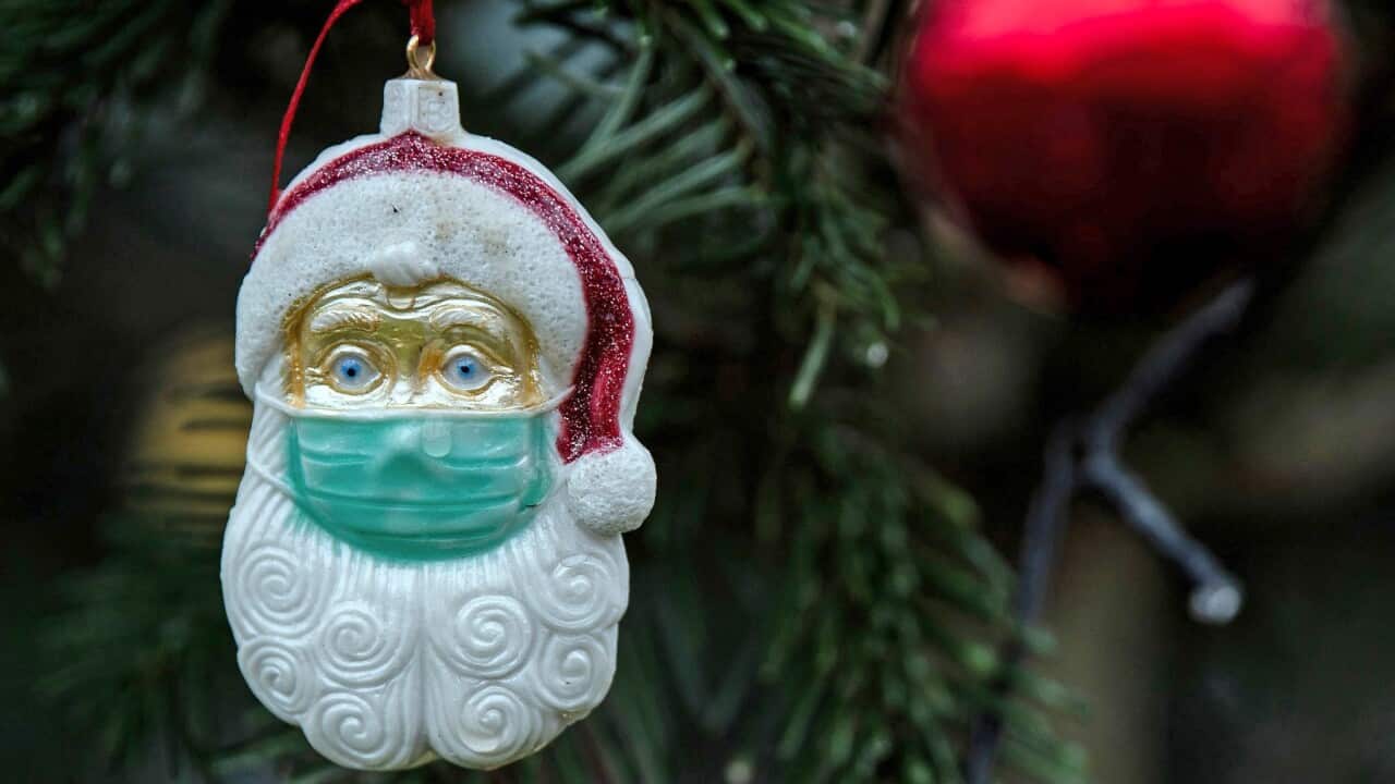 A Santa Claus with a protective mask decorates a Christmas tree in a front garden in Cologne, Germany