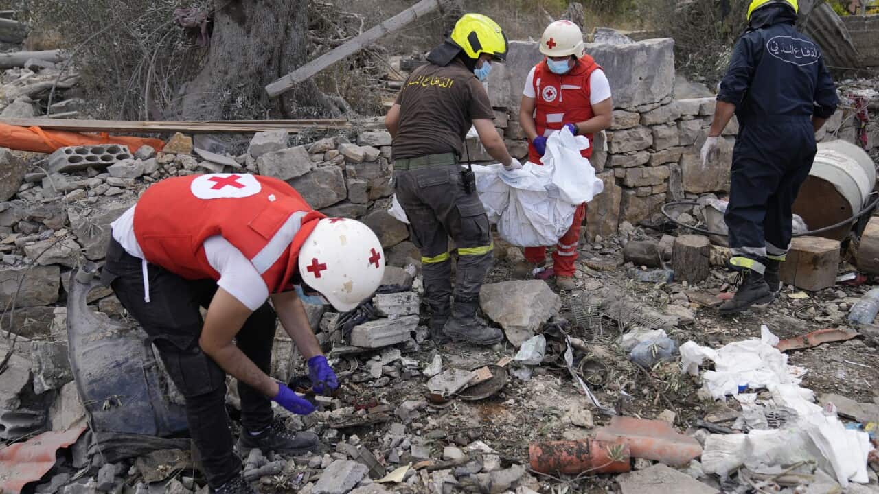 Personnel wearing vests and hard hats inspect rubble.