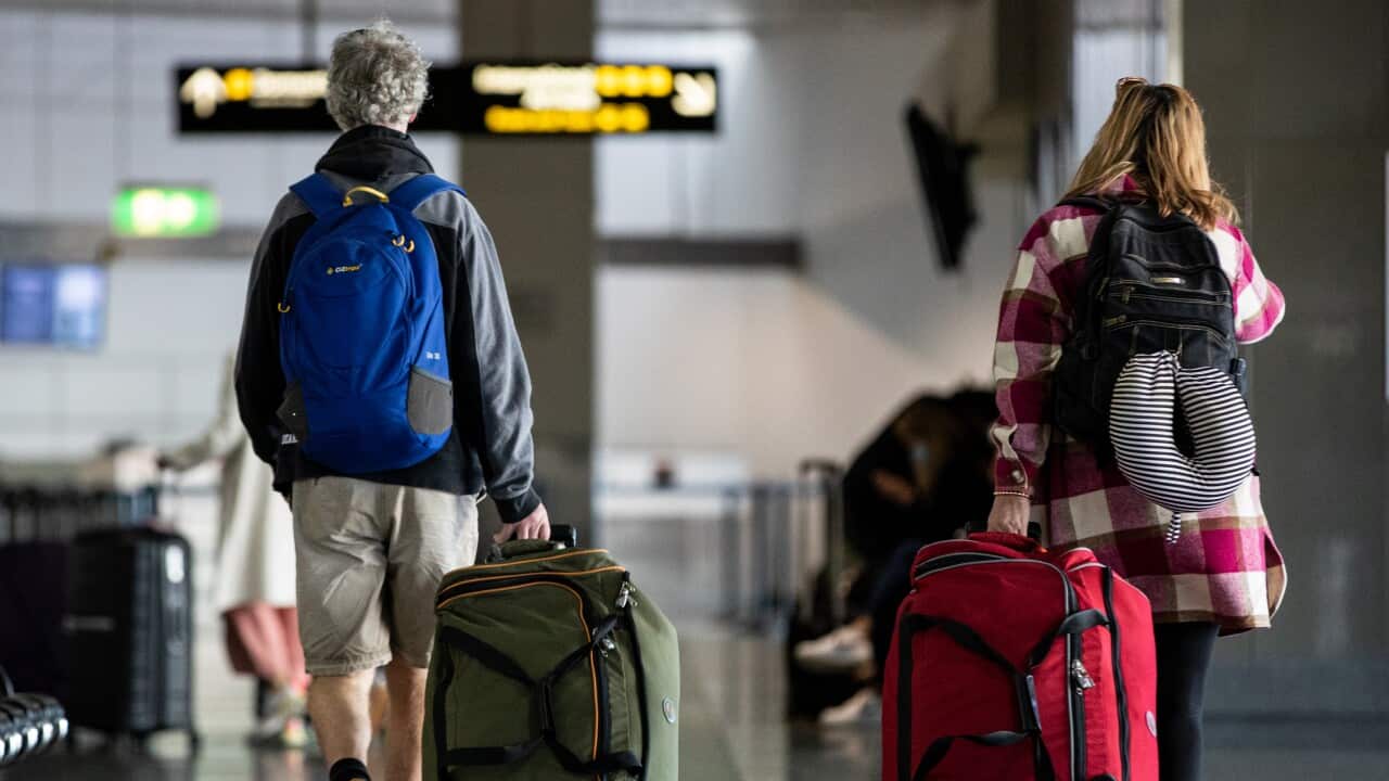 People walking through an airport, pulling wheeled luggage