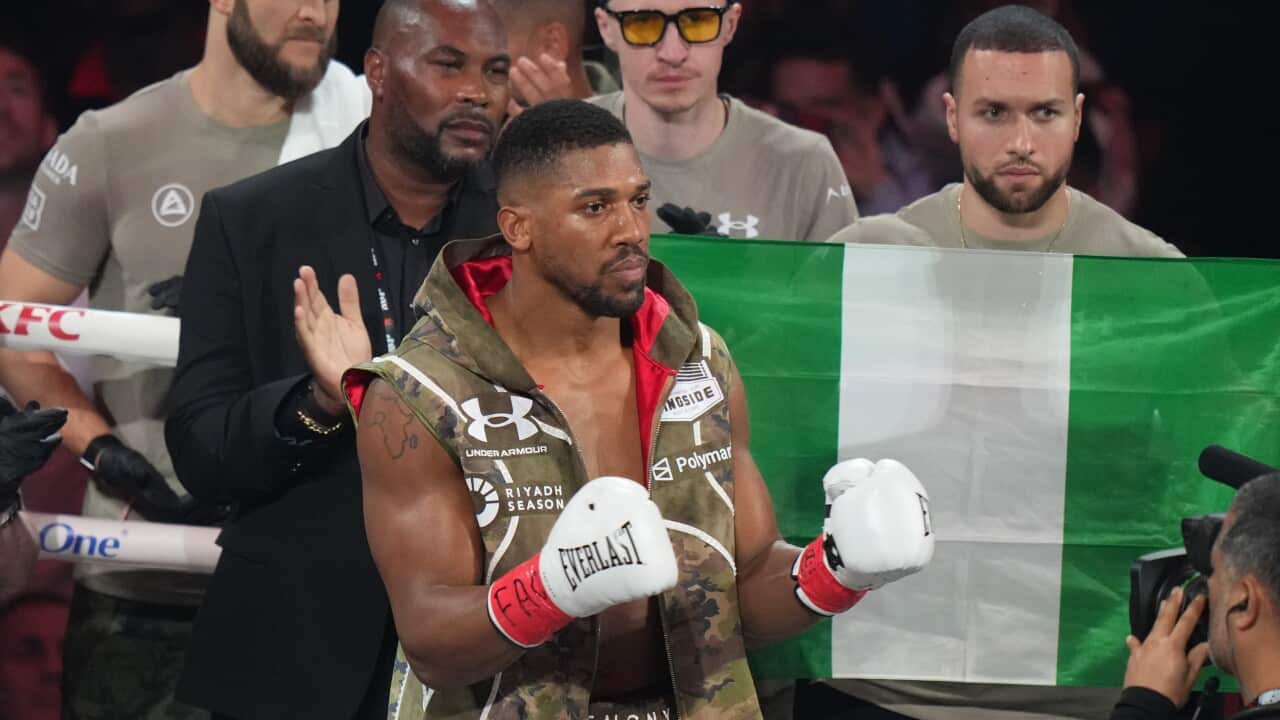 A boxer stands inside a ring with his team behind him.