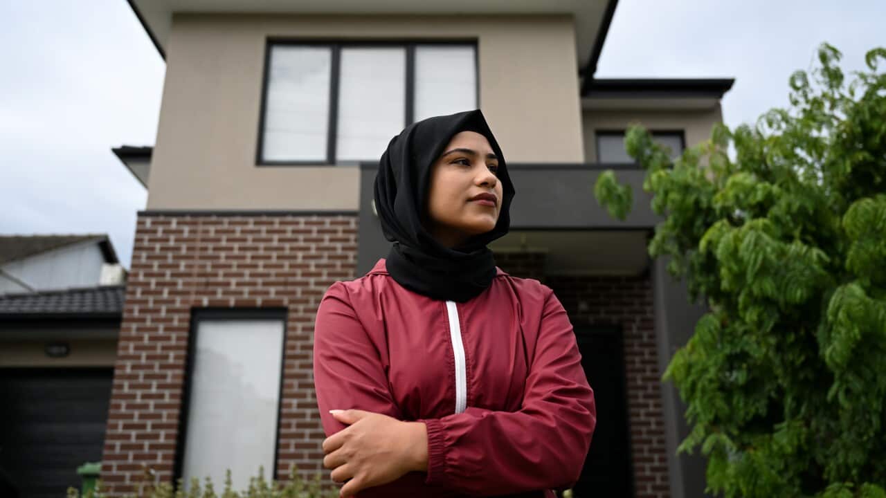 A woman in a headscarf looks on with a house seen in the background