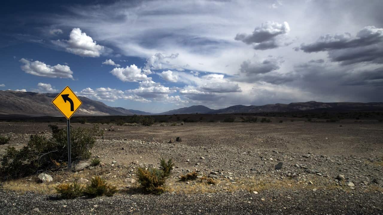 A traffic sign stands next to the road stretching through Death Valley, California.