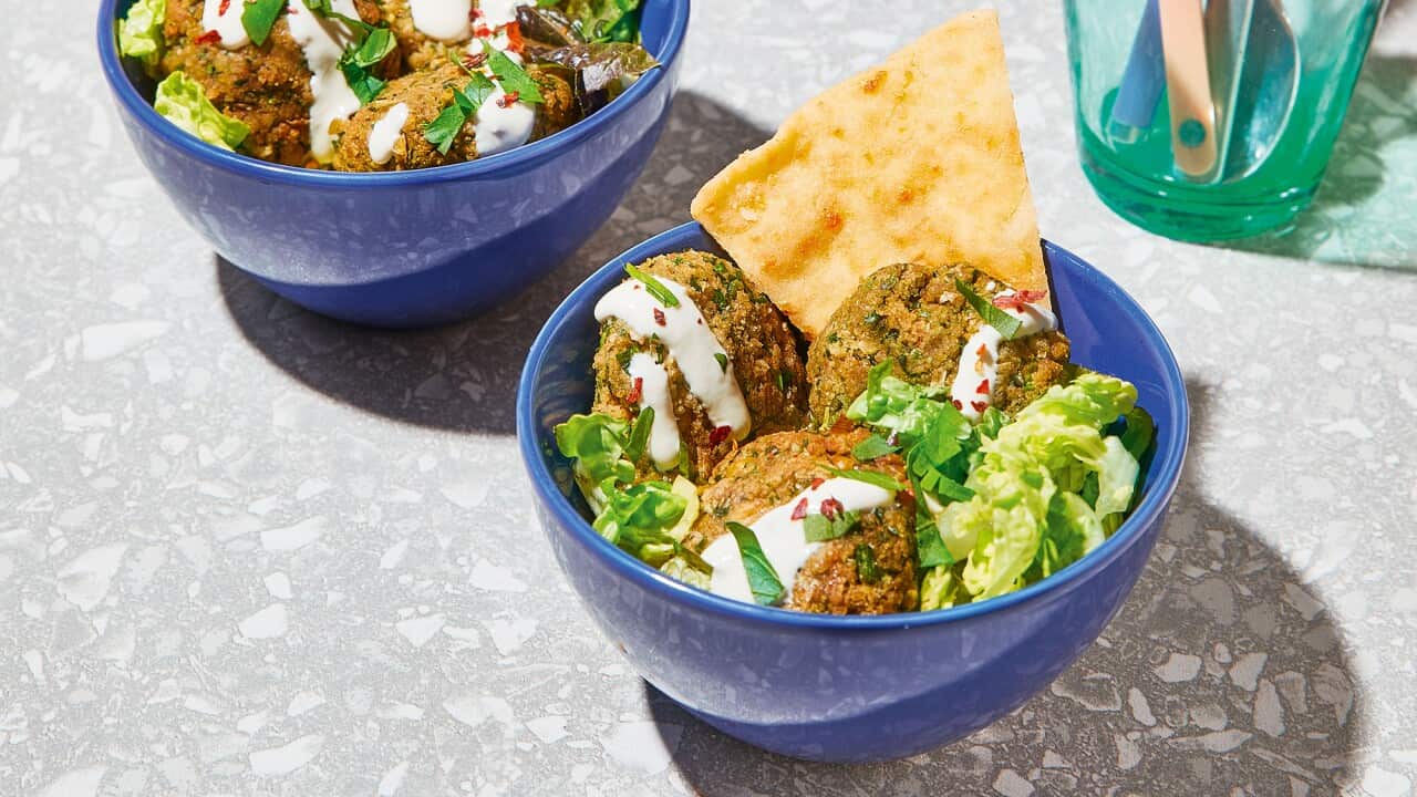 Three vibrant blue bowls sit on a grey surface. Each holds several falafel with salad, a cream sauce and flatbread pieces.