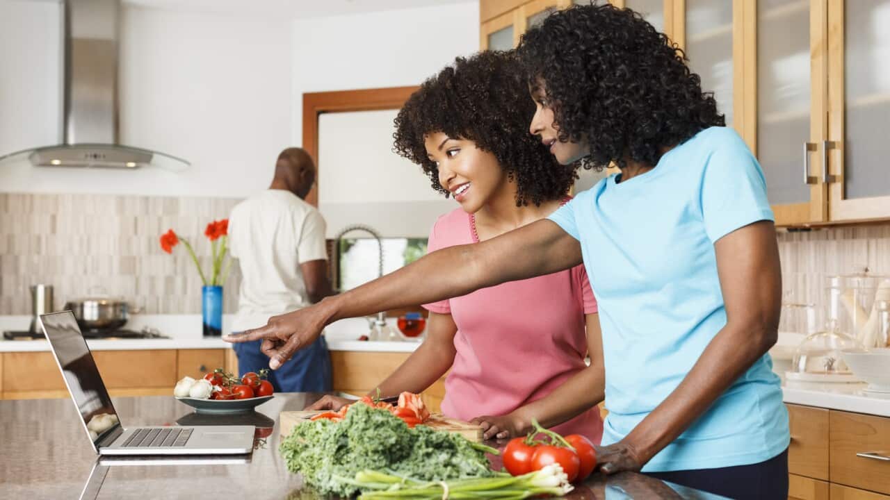 Black women using digital tablet and chopping vegetables in kitchen