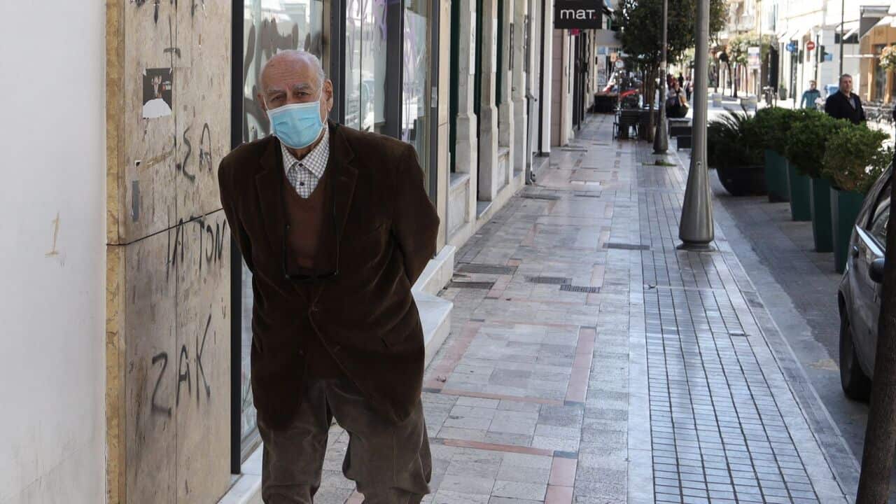 A Greek elderly man wearing a protective mask as a preventive measure, walking on an empty commercial street during the corona virus threat