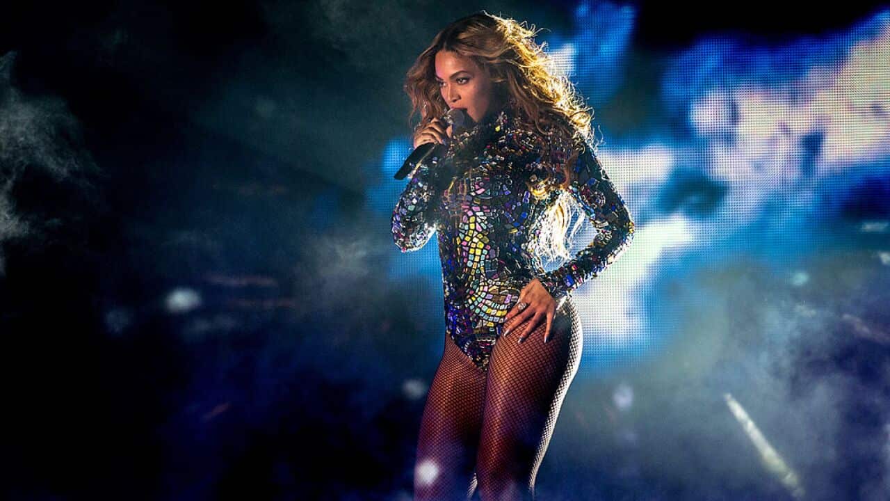 A woman in a metallic bodysuit is singing on stage.