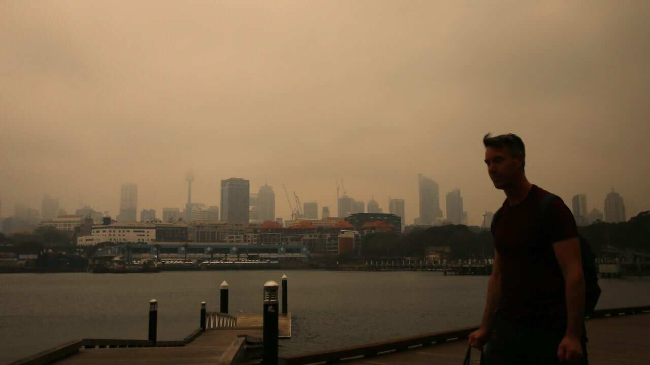 A man walks long the foreshore in Blackwattle bay as smoke haze from bushfires in New South Wales blankets the CBD in Sydney, Tuesday, December 10, 2019. (AAP Image/Steven Saphore) NO ARCHIVING