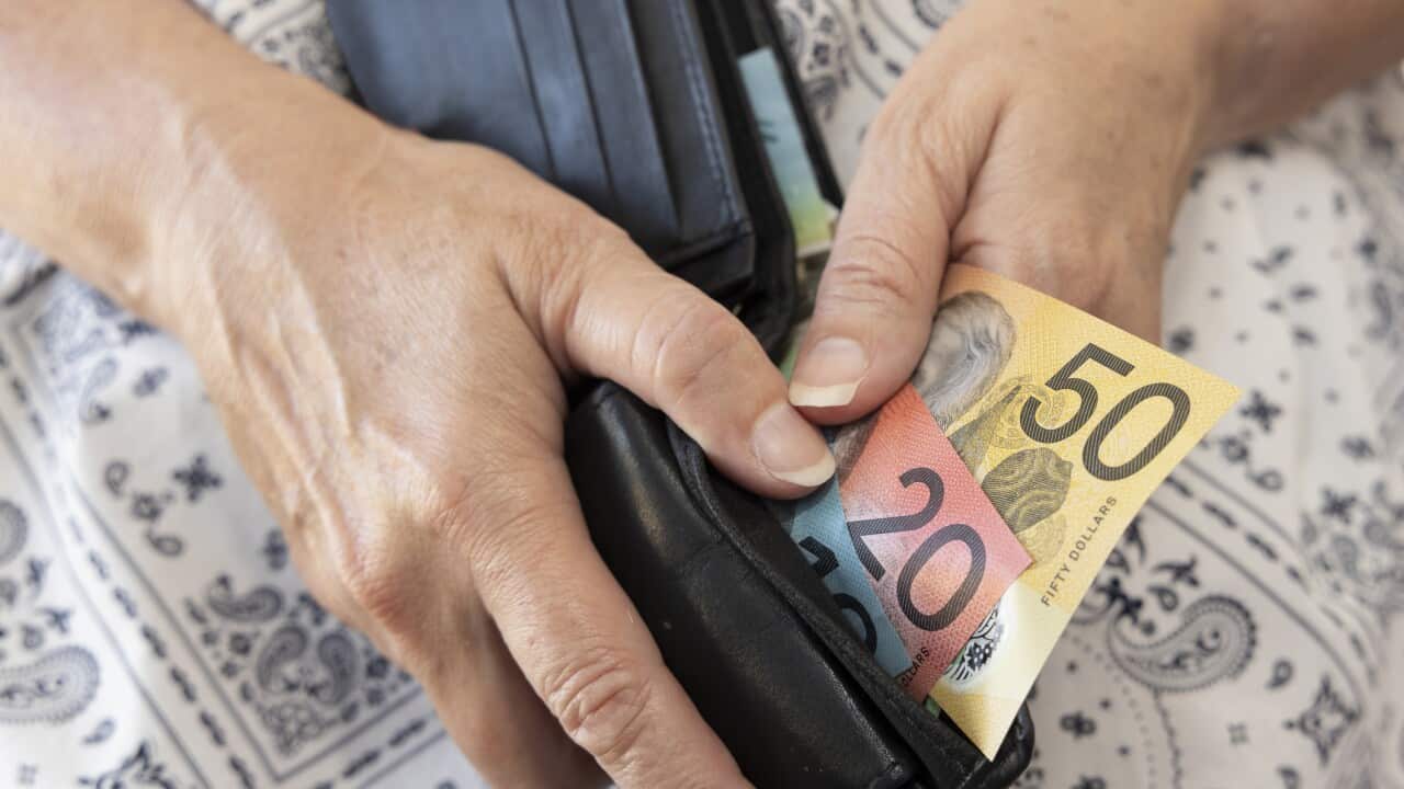 Mature adult holding a wallet containing some Australian bank notes.