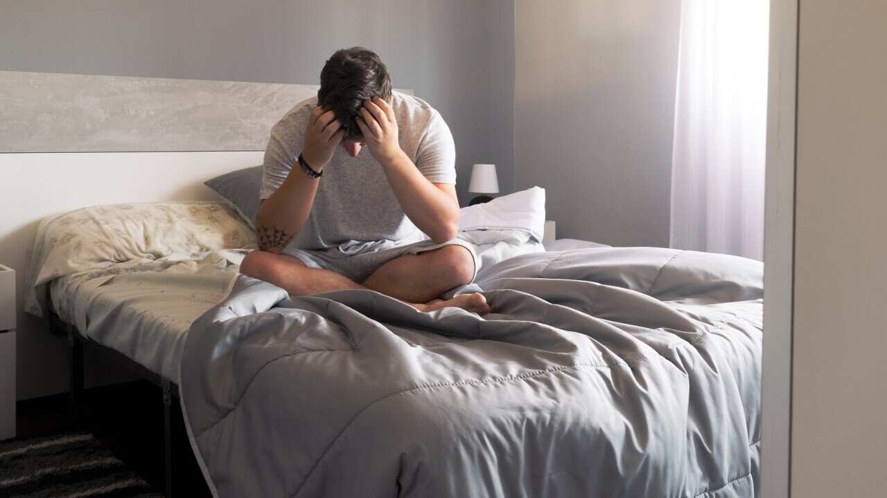 Portrait of a man sitting on a bed with his head in his hands