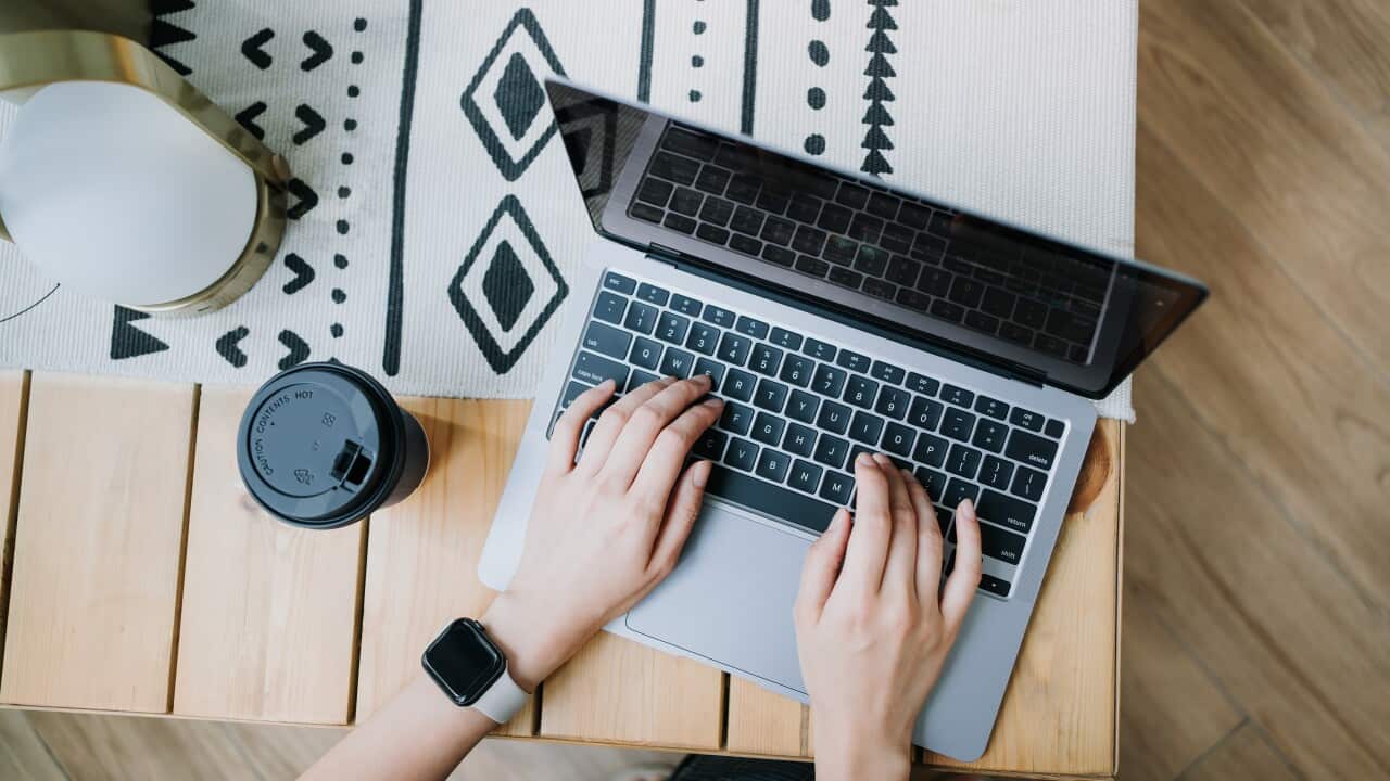High angle view of woman using laptop on wooden desk, with a cup of coffee by her side.