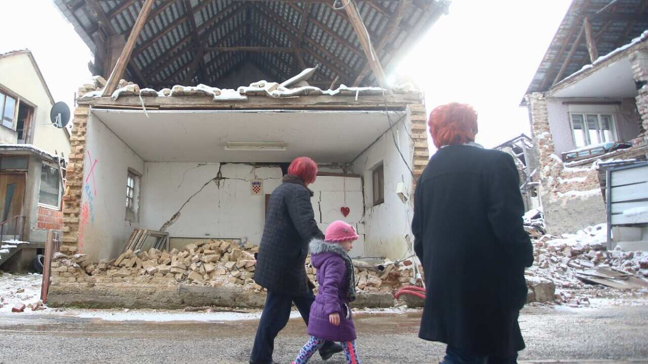 People passing by a collapsed house in the earthquake in the city center of Petrinja, Croatia