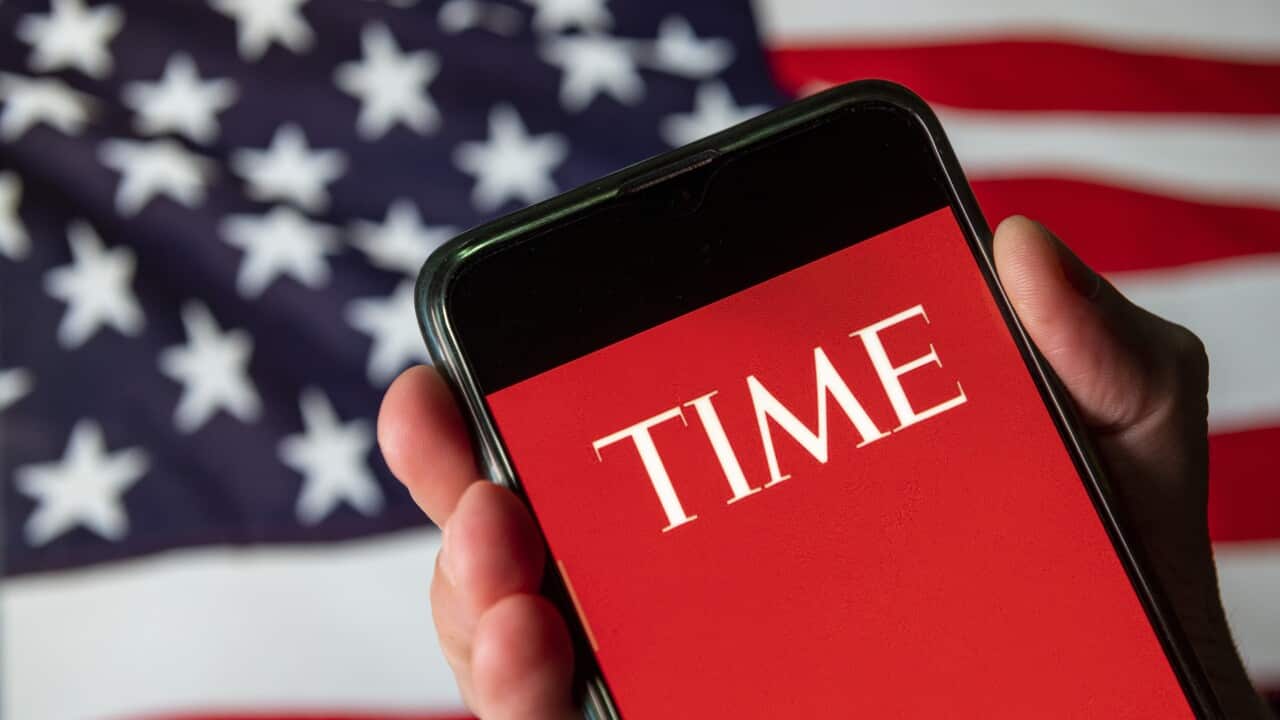 The Time magazine logo on a red background on a phone screen with the American flag behind it.